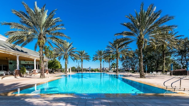 Una piscina con palmeras y sillas de descanso, rodeada por un edificio con columnas.