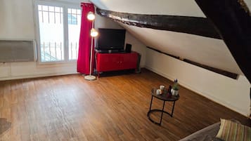 Een kamer met een schuine kap, een rode kast, een televisie, een klein rond tafeltje en een bank met gestreepte kussens.