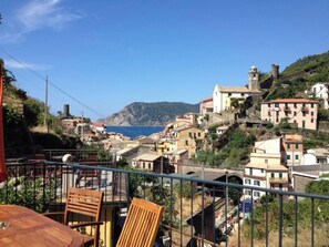 A balcony with a table and chairs overlooking a coastal village with buildings and a sea view. - Camere Giuliano Basso - Little Suite Sofia  (Vernazza)