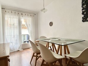 Een eethoek met een glazen tafel, witte stoelen, een plafondventilator en uitzicht op een balkon met planten.