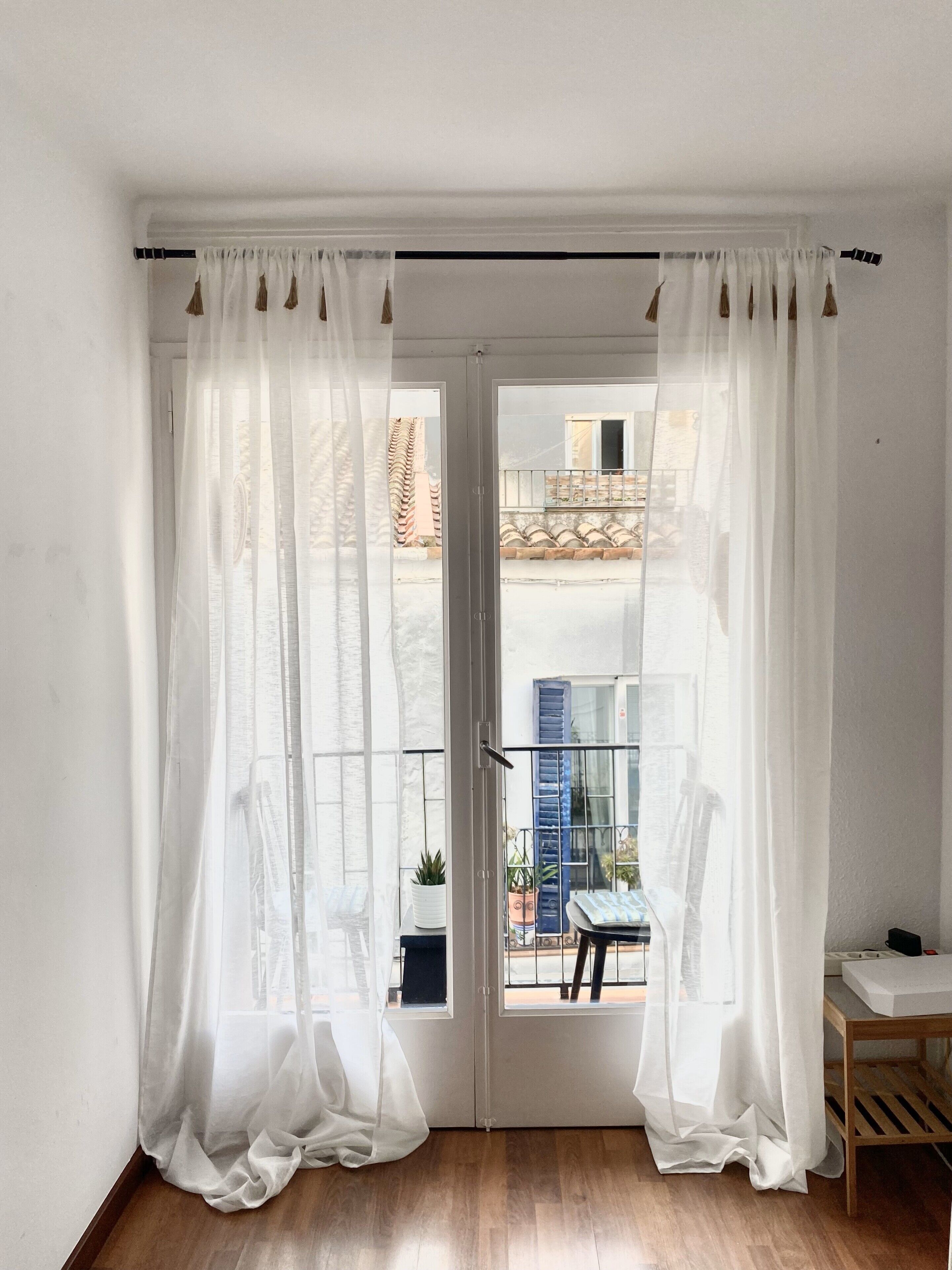 Een kamer met een schuifglasdeur die leidt naar een balkon. De kamer heeft een houten vloer en witte wanden.