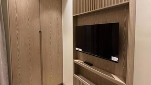 Une chambre moderne dotée d’une armoire en bois intégrée, d’un téléviseur à écran plat posé sur une étagère en bois et d’un éclairage encastré au plafond.