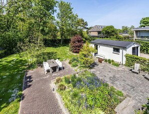 A residential property with a paved patio, a small white building with a dark roof, and a garden with various plants and a bench. - Koudekerke Coastal Getaway for 7 (Koudekerke)