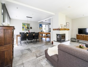 A modern living room with a fireplace, a dining area with a wooden table and chairs, and a television on a wooden cabinet. - Koudekerke Coastal Getaway for 7 (Koudekerke)