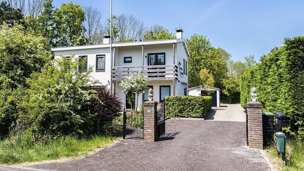 Kaksikerroksinen rakennus, jonka sisäänkäynti on portilla varustettu, ja jonka ympärillä on vehreää kasvillisuutta.