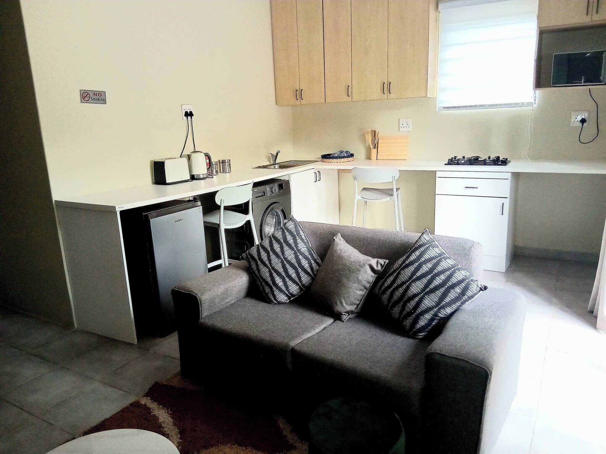 A compact living space with a sofa, a washing machine, a small kitchenette, and a dining area.
