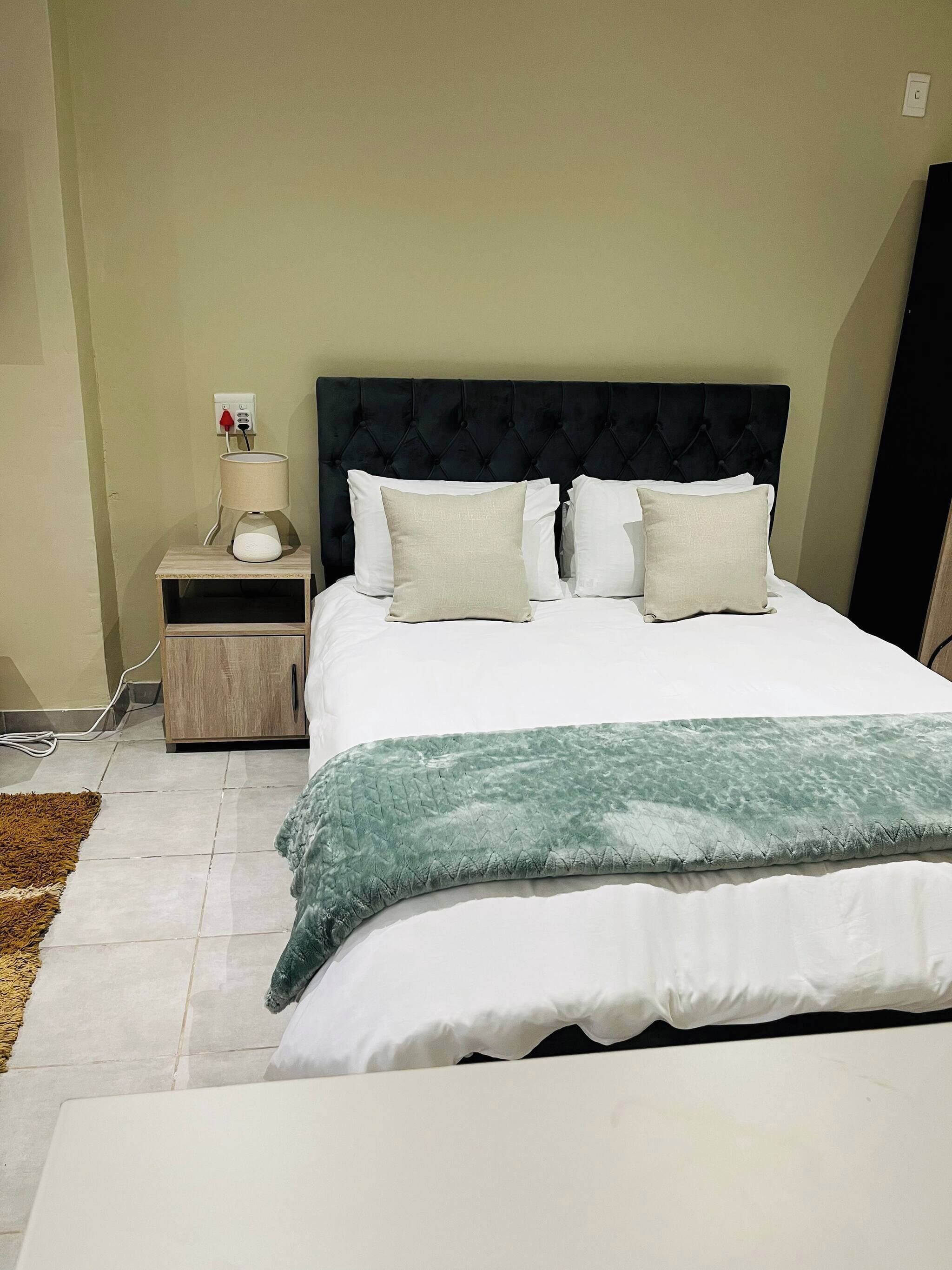 A bedroom with a bed, a nightstand, a lamp, and a power outlet.