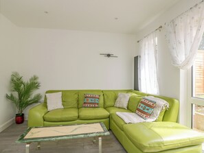A green sofa with patterned cushions, a small table, a potted plant, and a window with curtains. - 167 Leybourne Avenue (Bournemouth)