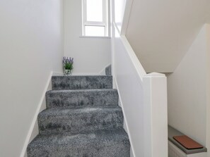 Una escalera con alfombra texturizada, una pequeña planta en maceta y un libro en un repisa.