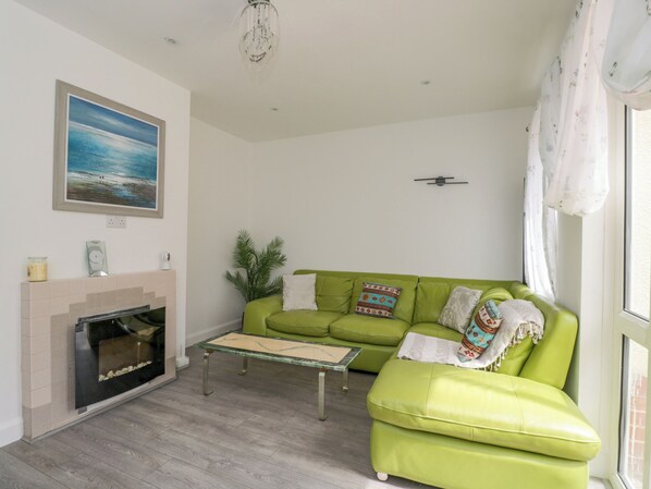 A living room with a green sofa, a fireplace, a painting, and a chandelier. - 167 Leybourne Avenue (Bournemouth)