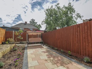 A backyard with a patio, a swing set, a wooden fence, and a house in the background. - 167 Leybourne Avenue (Bournemouth)