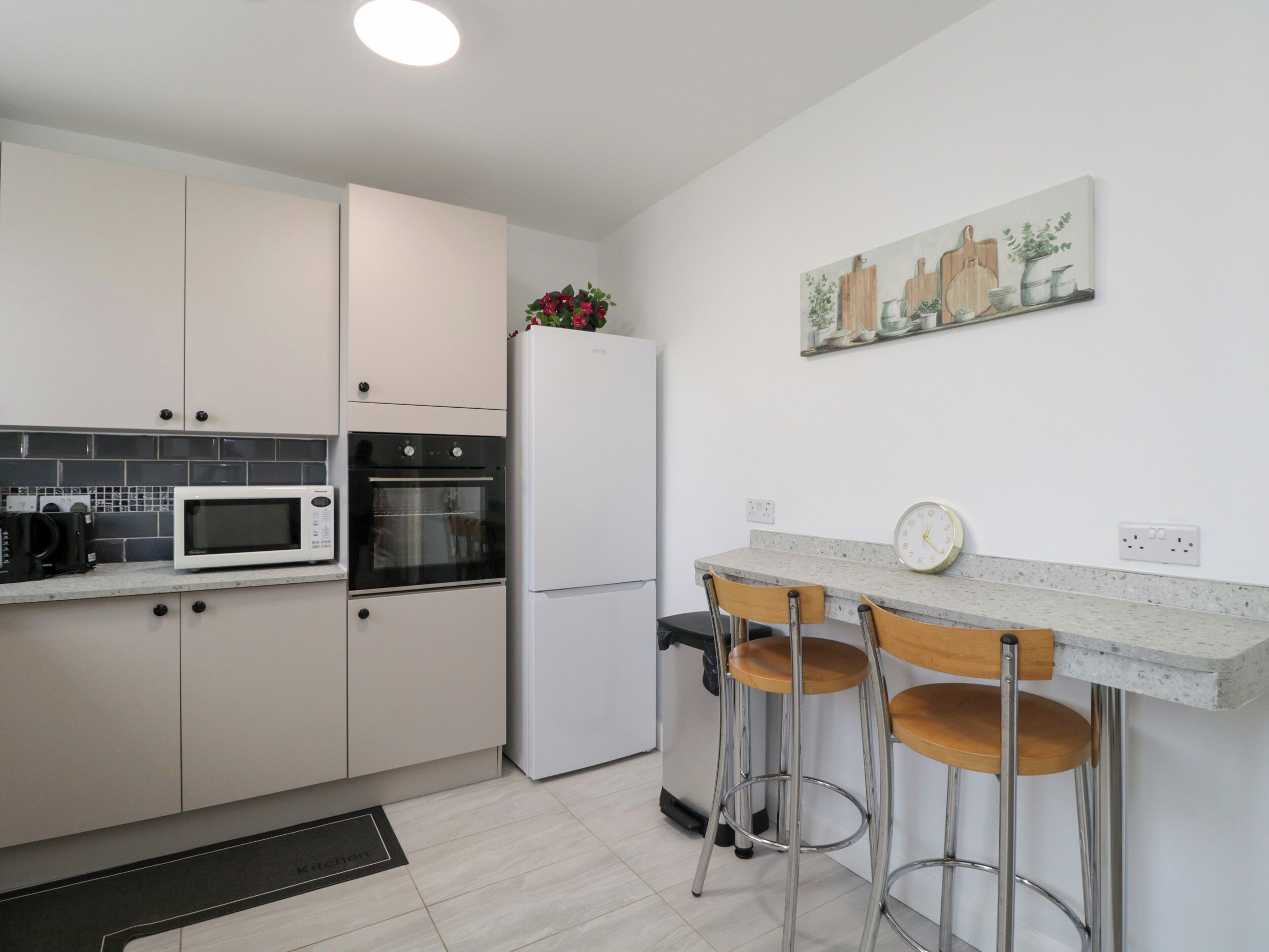 A modern kitchen with white cabinets, a microwave, an oven, a refrigerator, and a bar area with stools.