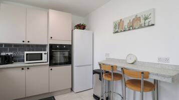 A modern kitchen with white cabinets, a microwave, an oven, a refrigerator, and a bar area with stools.