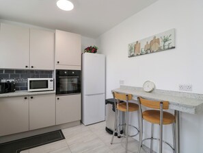 A modern kitchen with white cabinets, a microwave, an oven, a refrigerator, and a bar area with stools. - 167 Leybourne Avenue (Bournemouth)