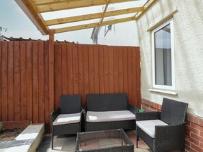 A covered patio area with two wicker chairs and a glass table, wooden fence, and a window. - 167 Leybourne Avenue (Bournemouth)