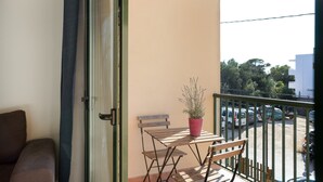 En balkon med et træbord, en stol, en potteplante og udsigt til parkerede biler og bygninger.