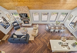 A spacious living area with a fireplace, a dining table, and multiple windows providing views of the outdoors. - NEW! Heated Pool, Hot Tub, Pickleball, Games, EV (Broken Bow)