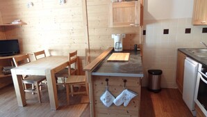 Een kleine keuken met houten keukenkastjes, een eettafel, stoelen, een koffiezetapparaat en een vaatwasser.