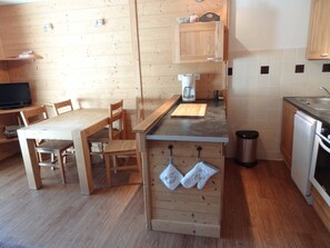 A compact kitchen with wooden cabinetry, a dining table, chairs, a coffee maker, and a dishwasher. - Ski-in/ski-out studio (La Salle-les-Alpes)