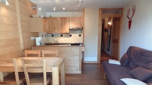 Een gezellige woonkamer met een houten eettafel en stoelen, een bank en een klein houten bijzettafeltje.