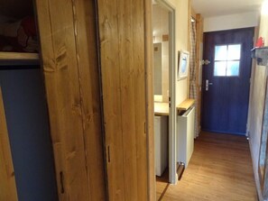 A narrow hallway with wooden flooring, a door with a window, and a small kitchen area visible through an open door. - Ski-in/ski-out studio (La Salle-les-Alpes)