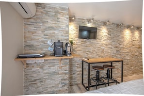 Ein gemütlicher Raum mit Steinwand, Flachbildfernseher, Kaffeemaschine, Waage und einem kleinen Tisch mit Hocker.