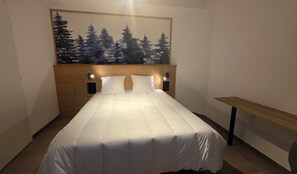 A neatly made bed with a headboard, a wall-mounted painting of trees, and a wooden bench. - Apartment with terrace in Briançon (Briançon)