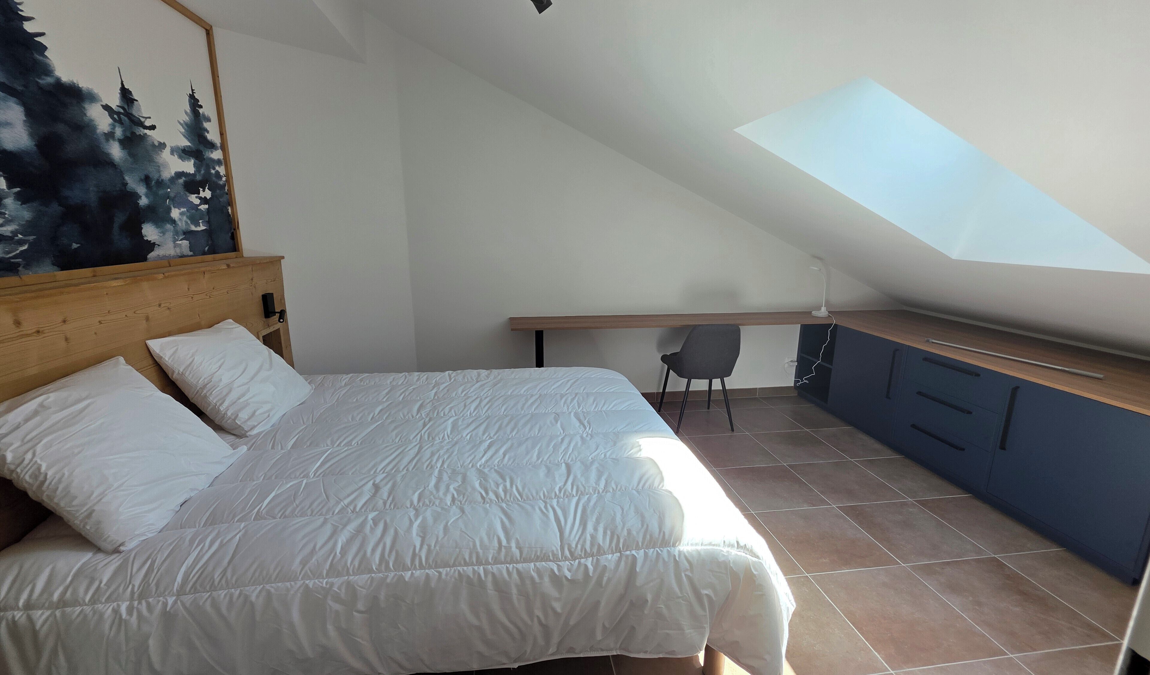 Une chambre à coucher avec un lit, un bureau, une chaise et une lucarne.