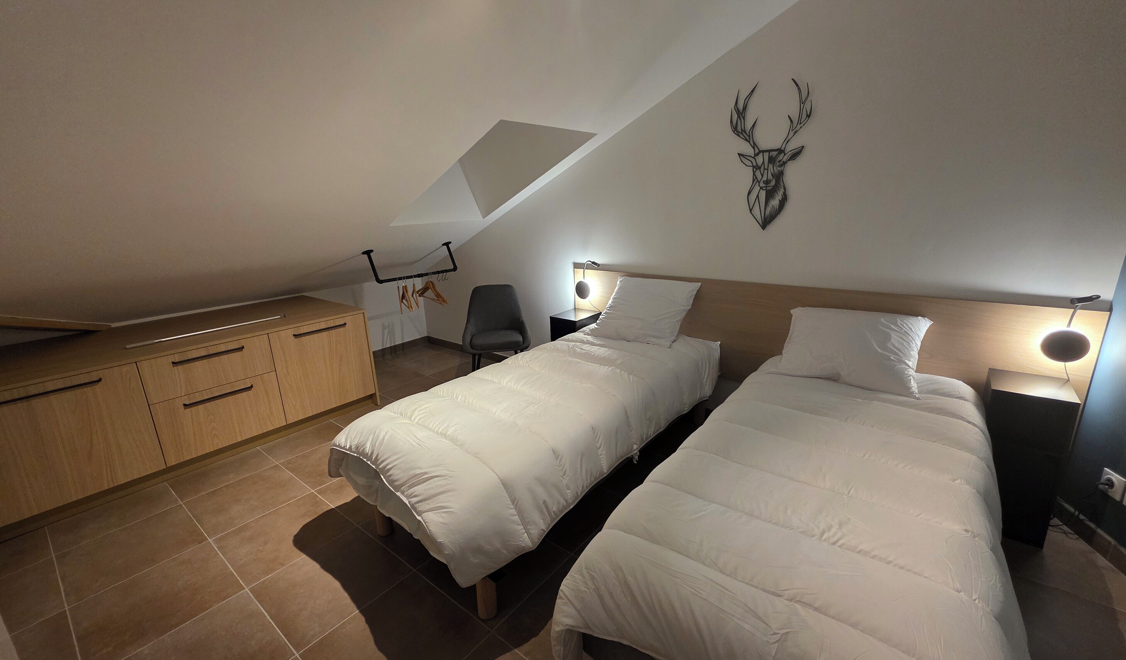 Une chambre avec deux lits, une armoire en bois, une chaise, un bureau et une décoration murale représentant une tête de cerf.