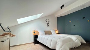 Una camera da letto con una finestra a lucernario, un letto con copriletto bianco, una decorazione con testa di cervo appesa al muro e una parete decorata in blu.