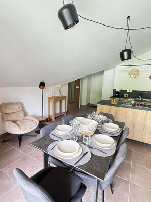 A dining area with a table set for four, a chair, a small side table, and a kitchen area with a sink and countertop. - Apartment with terrace in Briançon (Briançon)