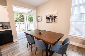 Ein Essbereich mit einem Holztisch, vier Stühlen, einer Kaffeemaschine und einem gerahmten Bild an der Wand.