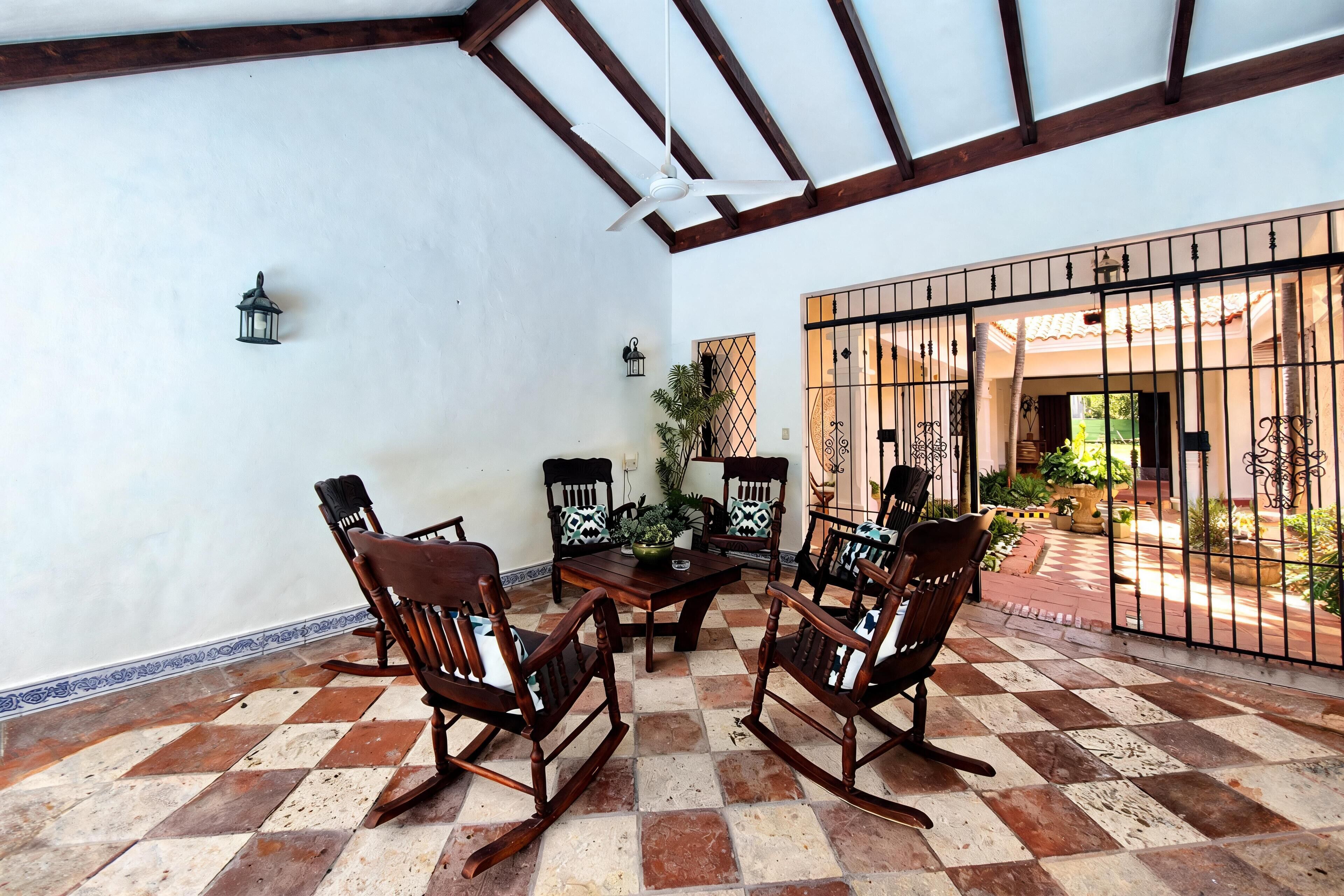 A patio with a checkered floor, wooden rocking chairs, a table, and a ceiling fan.