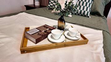 A bed with a tray containing a book, two cups, and a vase with flowers.