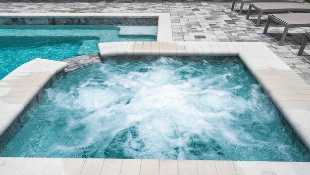 Ett bubbelbad med en kakelbeklädd uteplats, utomhusmöbler och en pool.