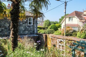 A stone building with a window, surrounded by greenery and a palm tree. - Gorway Cottage (Teignmouth)