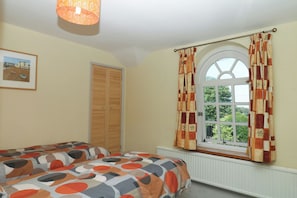 A bedroom with a bed, a window with curtains, a radiator, and a door. - Gorway Cottage (Teignmouth)