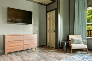 Ein Zimmer mit einem hölzernen Schminktisch, einem an der Wand befestigten Fernseher, einer Tür, einem Stuhl und einem kleinen Tisch.
