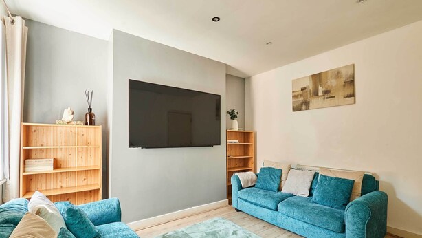 Una sala de estar con un sofá azul, estanterías de madera, un televisor de pantalla plana y un cuadro en la pared.