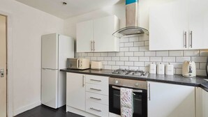 Una cocina moderna con gabinetes blancos, estufa a gas, horno empotrado y refrigerador.