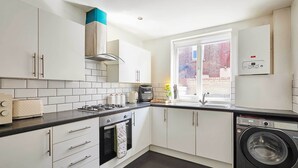 Una cocina moderna con armarios blancos, horno empotrado, lavadora y ventana con vistas.