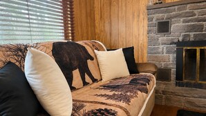 Ein Sofa mit Bär-Motiv, ein Kamin aus Stein und Holzvertäfelung.