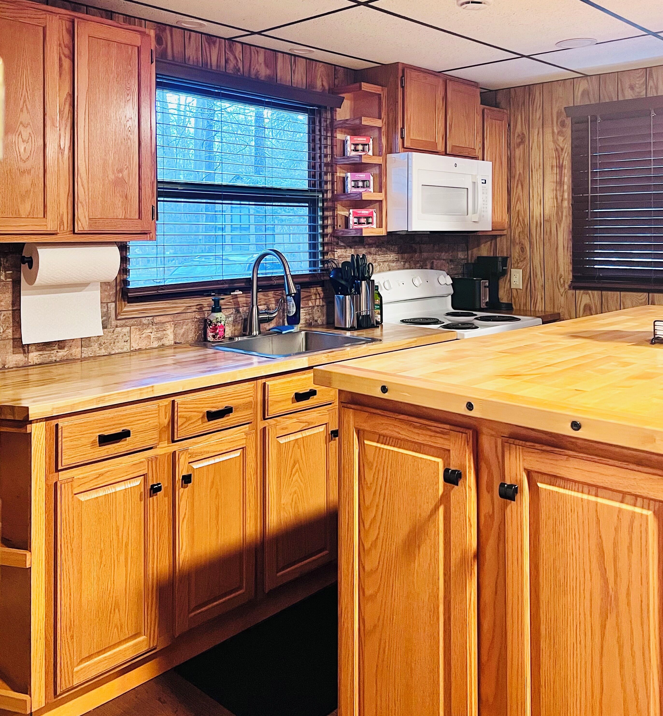 A kitchen with wooden cabinets, a stainless steel sink, a white stove, and a window with blinds.