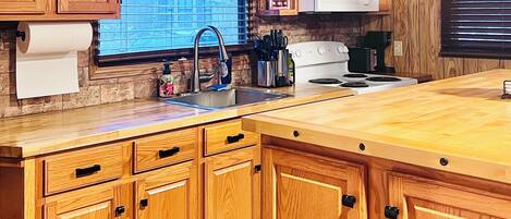 A kitchen with wooden cabinets, a stainless steel sink, a white stove, and a window with blinds.