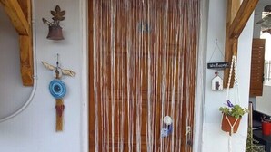 Uma porta de madeira com uma placa acima, uma cortina de macramé, uma placa de boas-vindas e um pequeno vaso com planta à direita.