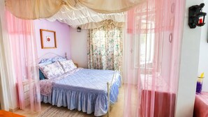 Quarto com cama, mesa de cabeceira, luminária na parede e janela com cortinas.