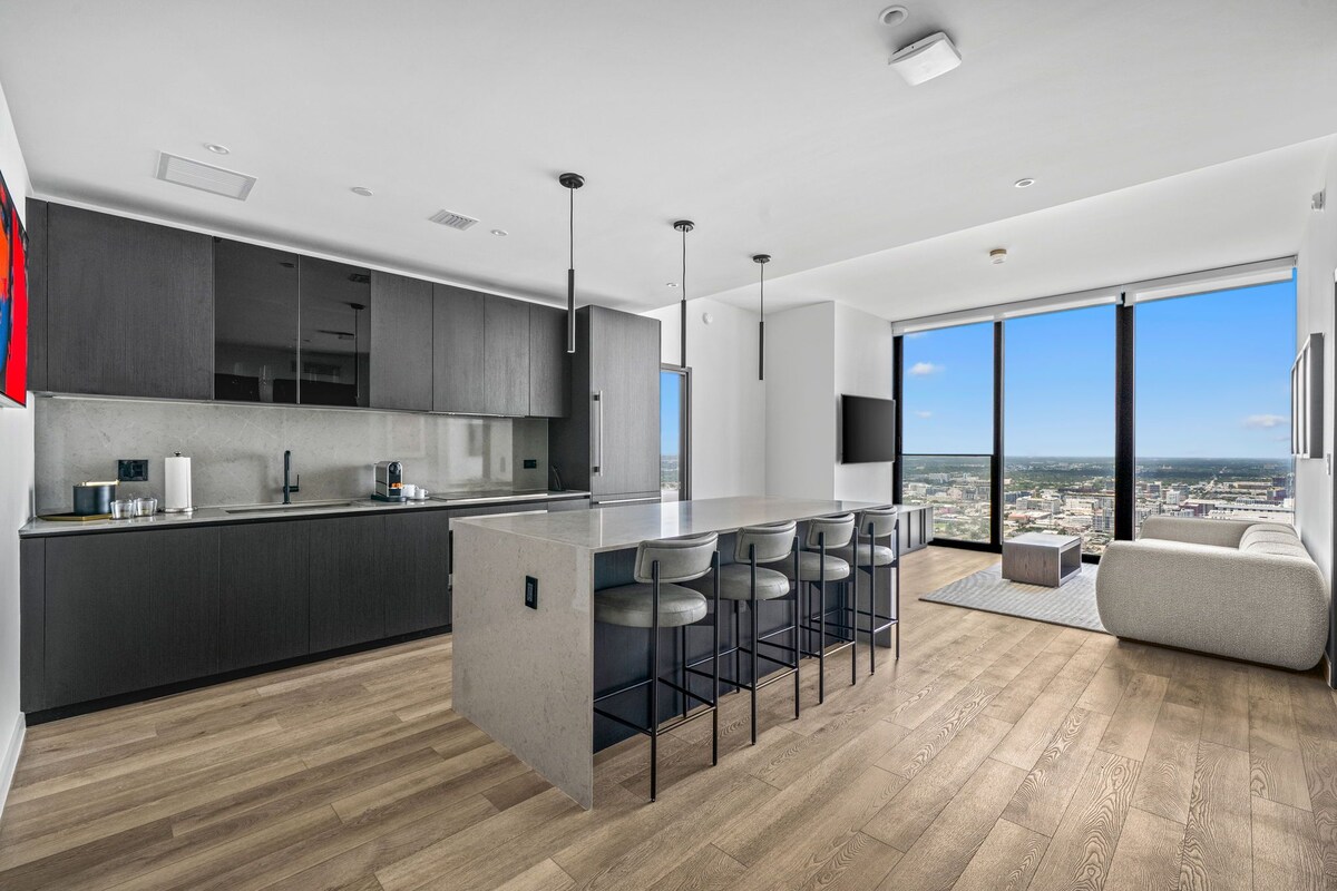 A modern kitchen with a central island, bar stools, and a large window offering a city view.