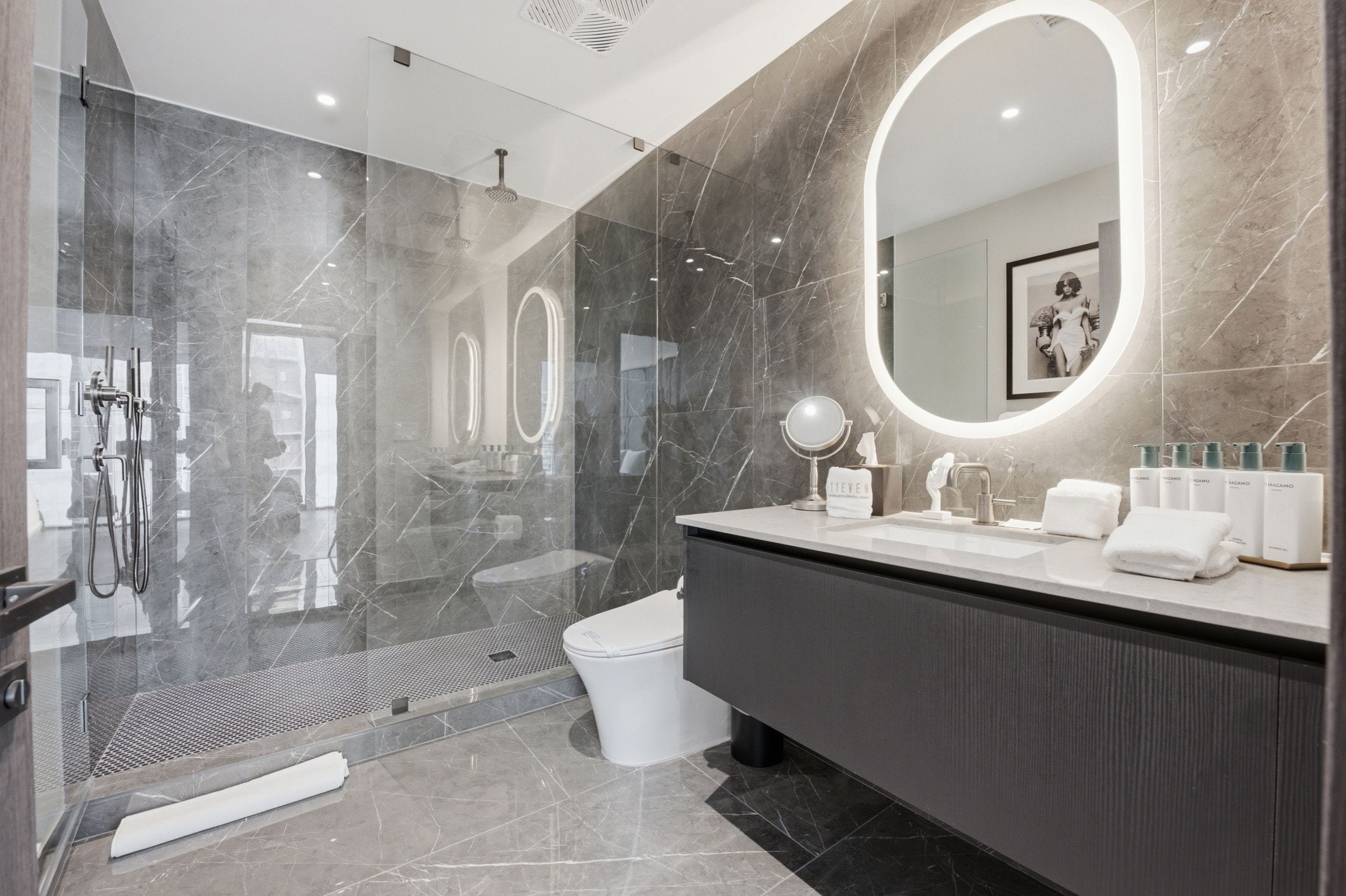 A modern bathroom with a large mirror, a shower area, and a vanity with toiletries.