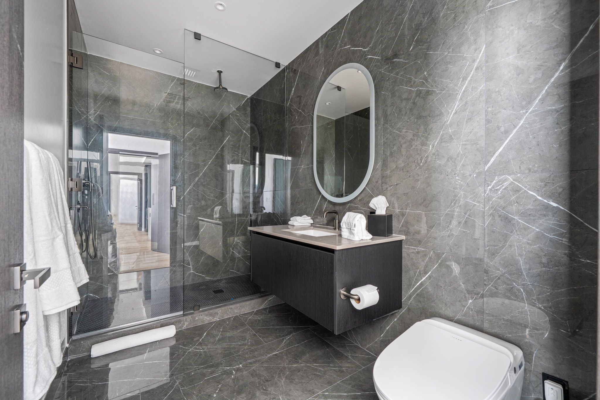 A modern bathroom with a glass shower enclosure, a dark marble vanity, and a white toilet.