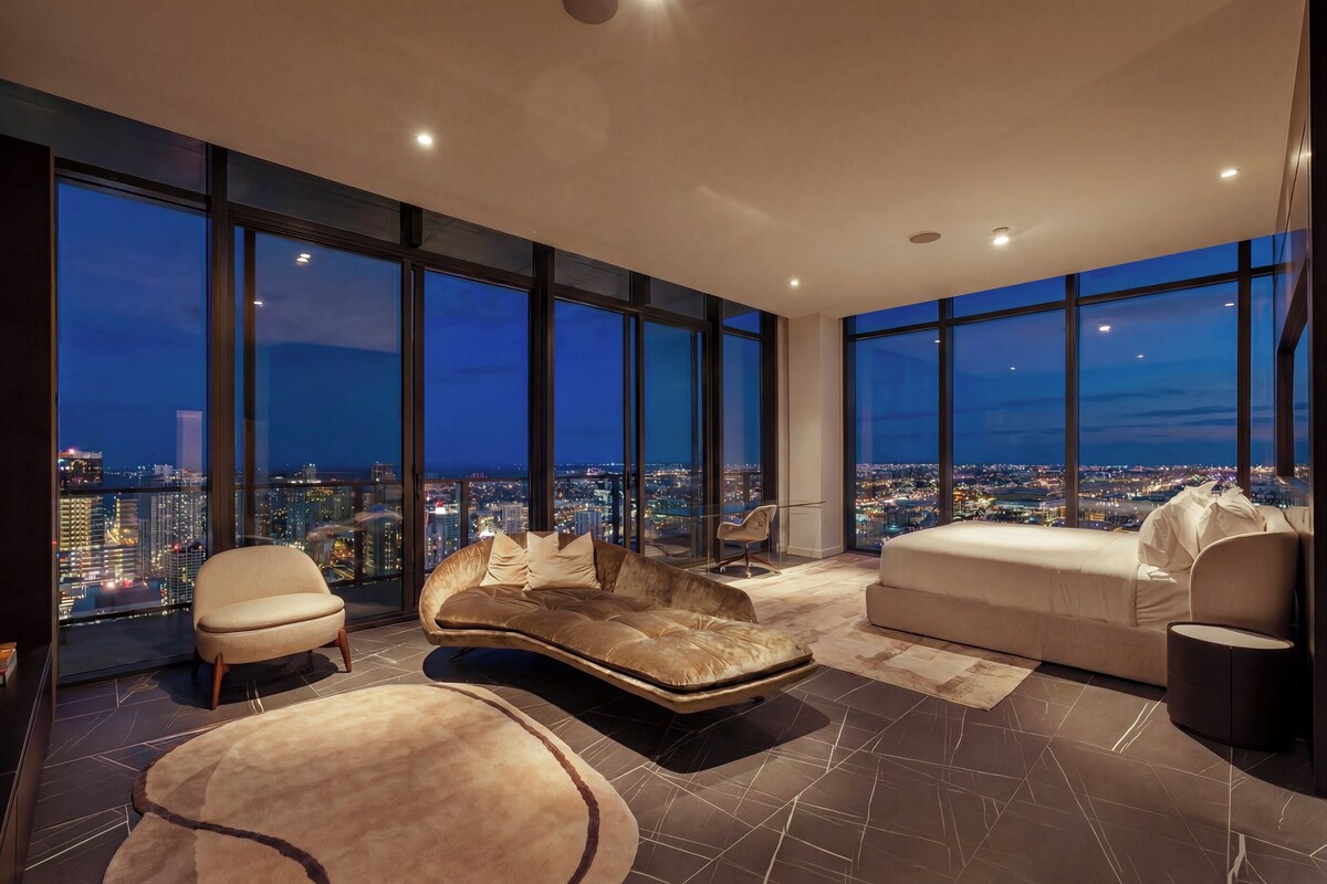A high-rise interior with large windows, a curved sofa, a round ottoman, and a chair.